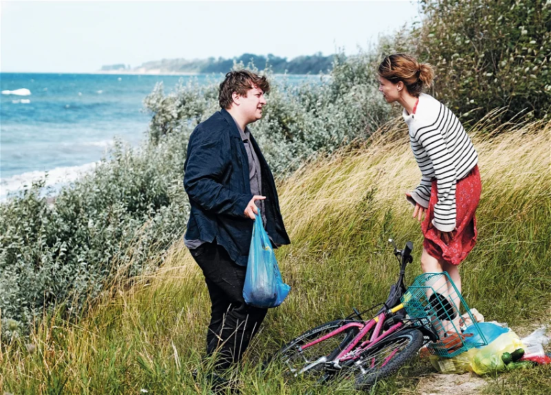 Christian Schubert als Leon und Paula Beer stehen sich in ROTER HIMMEL von Christian Petzold an der Ostsee gegenüber. Er hält einen Plastiksack mit Gulasch in der Hand. Sie ist gerade mit ihrem Fahrrad gestürzt.