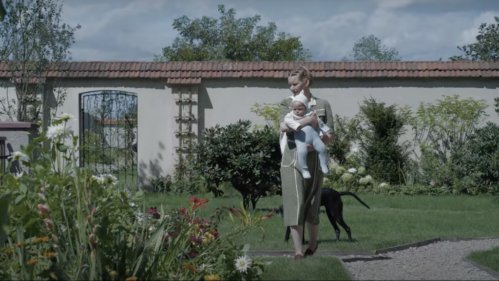 Sandra Hüller als Hedwig Höß spaziert mit Kind im Arm durch ihren Blumengarten. 